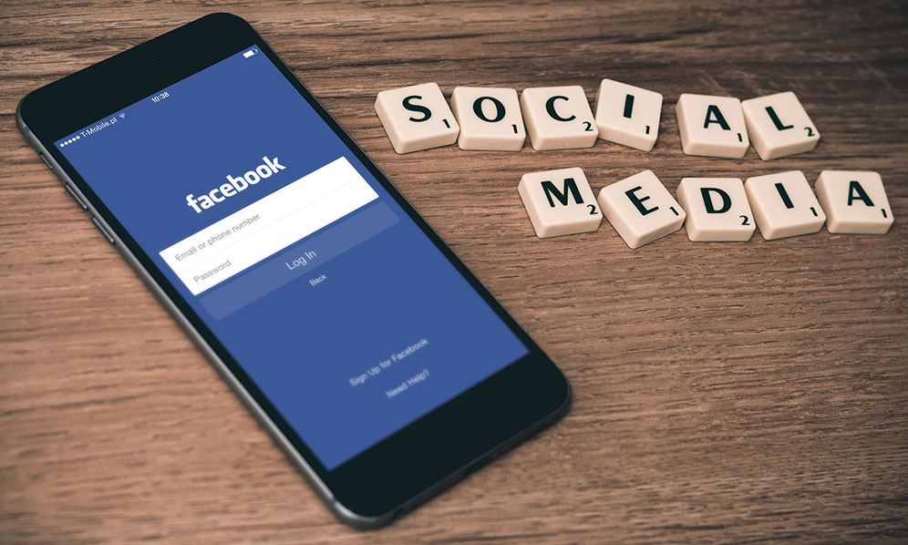 mobile phone showing Facebook with scrabble tiles at right spelling out social media